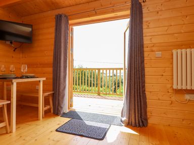 A wooden interior room with an open door leading to a balcony and a table set with glasses and plates at Northwood Lodge in Llanbedrog