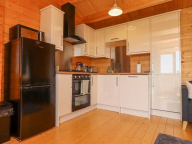 A kitchen with black refrigerator microwave oven stove white cabinets and wooden floor at Northwood Lodge in Llanbedrog