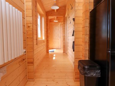 A wooden hallway with a window and a door at the end with a trash bin and a black refrigerator on one side at Northwood Lodge in Llanbedrog
