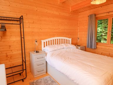 A bedroom with a white bed and bedside tables next to a window with curtains at Northwood Lodge in Llanbedrog