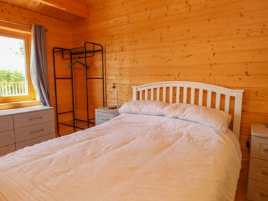 A bedroom with a white bed against wooden walls and gray furniture near a window at Northwood Lodge in Llanbedrog