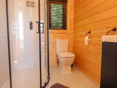 A bathroom with a corner shower cubicle, toilet, and a wall with a window at Northwood Lodge in Llanbedrog