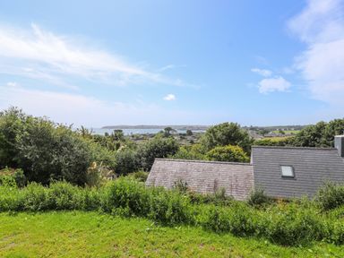 A view of rooftops trees and a body of water under a blue sky at Northwood Lodge in Llanbedrog