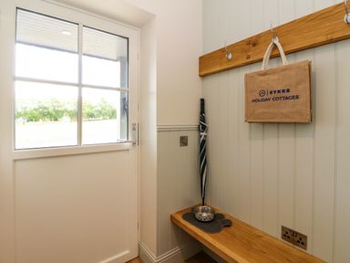 An entryway with a glass panel door a wooden bench an umbrella dog bowl and a hanging bag at Strawberry Cottage in Wester Essendy near Dunkeld