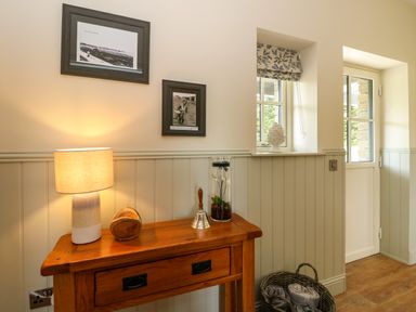 A wooden console table with a lamp a wooden bowl a hand bell and a glass vase in a room with two windows a basket on the floor at Strawberry Cottage Wester Essendy near Dunkeld