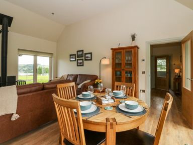 A dining area with a wooden table set for four and a living room with brown leather sofas at Strawberry Cottage Wester Essendy near Dunkeld