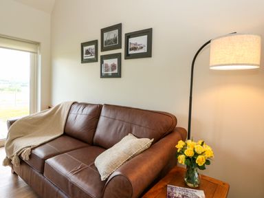 A living room with a brown leather sofa a beige throw and cushion a wooden side table with yellow flowers and a lamp on Strawberry Cottage Wester Essendy near Dunkeld