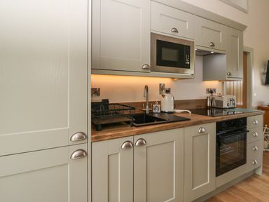 A kitchen with grey cabinets a microwave oven toaster kettle and sink at Strawberry Cottage Wester Essendy near Dunkeld