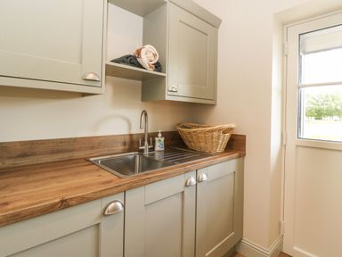 A utility room with a stainless steel sink wooden countertop a wicker basket and folded towels on shelves at Strawberry Cottage in Wester Essendy near Dunkeld