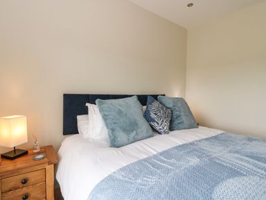 A bedroom with a bed with blue and white bedding and a wooden nightstand with a lamp and diffuser at Strawberry Cottage Wester Essendy near Dunkeld