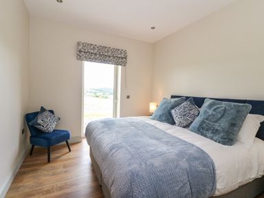 A bedroom with a bed with blue pillows and blanket a blue chair with a cushion wooden floor and a window at Strawberry Cottage in Wester Essendy near Dunkeld