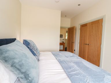 A bedroom with a bed with blue pillows and a blue throw next to wooden doors at Strawberry Cottage in Wester Essendy near Dunkeld