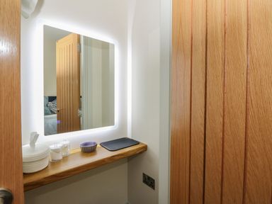 A bathroom vanity area with a lighted mirror wooden shelf tissue container cotton swabs and a small bowl at Strawberry Cottage Wester Essendy near Dunkeld