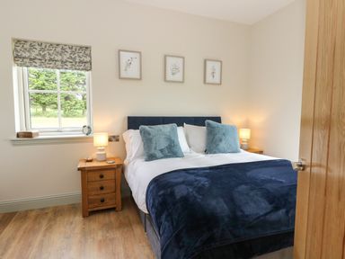 A bedroom with a double bed two bedside tables with lamps a window and three framed pictures on the wall at Strawberry Cottage in Wester Essendy near Dunkeld