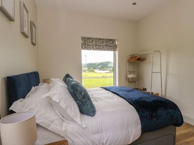 A bedroom with a bed pillows a standing rack with hangers and a window with a view of green fields at Strawberry Cottage Wester Essendy near Dunkeld