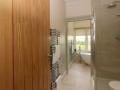 A bathroom with a wooden door towel rack shower and a freestanding bathtub near a window overlooking fields at Strawberry Cottage Wester Essendy near Dunkeld