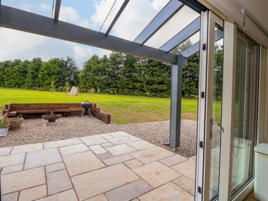 A patio with stone tiles and a fire pit with seating and a barbecue outside at Strawberry Cottage in Wester Essendy near Dunkeld