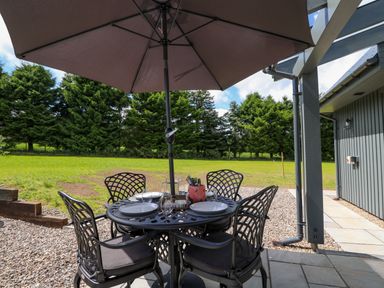 A patio dining area with metal table and chairs under a large umbrella in a backyard at Strawberry Cottage Wester Essendy near Dunkeld