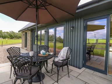 An outdoor patio with a table and four chairs under an umbrella next to a building with glass doors at Strawberry Cottage in Wester Essendy near Dunkeld