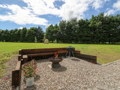 An outdoor seating area with a fire pit grill and plants on gravel with trees and grass in the background at Strawberry Cottage in Wester Essendy near Dunkeld