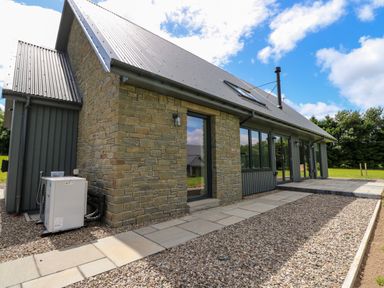 Exterior view of a stone and wood house with a metal roof and paved walkway at Strawberry Cottage in Wester Essendy near Dunkeld