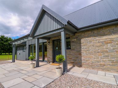 Front entrance of a house with stone and vertical wood panel exterior walls and potted plants at Bramble Cottage Wester Essendy near Dunkeld