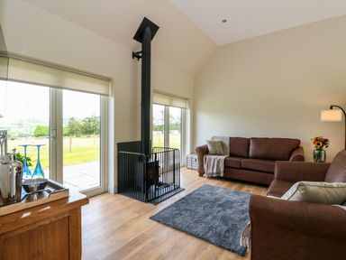 A living room with brown sofas a wood stove and large windows at Bramble Cottage Wester Essendy near Dunkeld