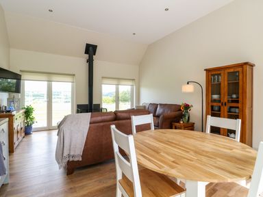 A living room with leather sofas round wooden dining table glass cabinet and wood burning stove at Bramble Cottage Wester Essendy near Dunkeld