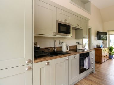 A kitchen with cabinets microwave oven sink toaster and a wooden sideboard with a television in the background at Bramble Cottage in Wester Essendy near Dunkeld