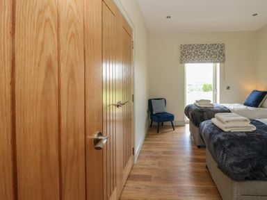 A bedroom with two single beds towels on beds a blue chair near window and wooden doors at Bramble Cottage Wester Essendy near Dunkeld