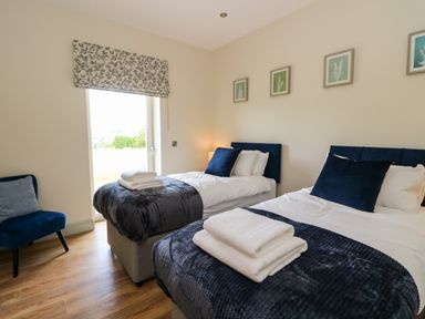 A bedroom with two single beds with navy blue throws and pillows a blue chair and framed pictures on the wall at Bramble Cottage in Wester Essendy near Dunkeld