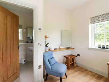 A room with a blue chair wooden stool wall shelf mirror and window with plants at Bramble Cottage in Wester Essendy near Dunkeld