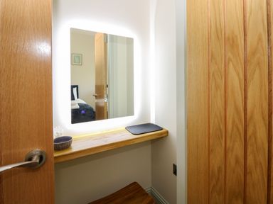 A small wooden vanity with a backlit square mirror a closed door and a wooden stool at Bramble Cottage Wester Essendy near Dunkeld