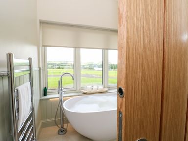 A bathroom with a freestanding bathtub near windows and a chrome towel rail with a white towel at Bramble Cottage Wester Essendy near Dunkeld
