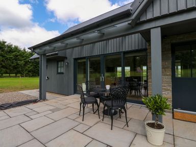 An outdoor patio with a round metal table and four chairs next to large glass sliding doors and a potted plant at Bramble Cottage in Wester Essendy near Dunkeld