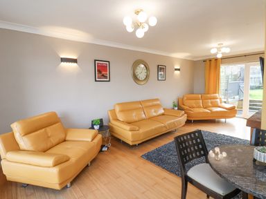 A living room with three yellow sofas a round dining table and chairs a rug wall clock and posters at 315 Filey Road Scarborough