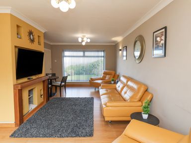 A living room with yellow sofas a wall clock a television above a fireplace and a gray rug at 315 Filey Road Scarborough