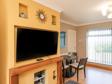 A living area with a wall-mounted television above a wooden mantel and a dining table with chairs near a window with vertical blinds at 315 Filey Road Scarborough