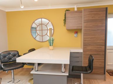 A kitchen area with a white countertop island black bar stools a round wall mirror and wooden cabinets at 315 Filey Road Scarborough