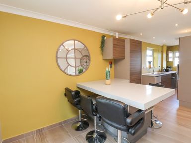A kitchen with a breakfast bar and black bar stools with a circular mirror on a yellow wall at 315 Filey Road in Scarborough