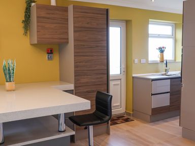 A kitchen with yellow walls wooden cabinets a black chair a plant on the counter and a door at 315 Filey Road Scarborough