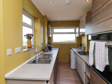 A kitchen with yellow walls a double sink a kettle flowers in a vase and two windows at 315 Filey Road in Scarborough