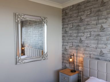 A bedroom corner with a bed with a tufted headboard beside a nightstand with a lamp and a large ornate mirror on the adjacent wall at 315 Filey Road Scarborough