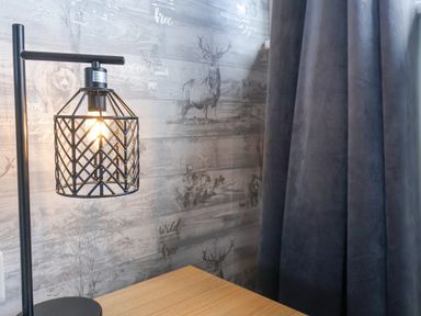 A table lamp with a cage-style shade on a wooden surface near a wallpapered wall with animal illustrations and dark curtains at 315 Filey Road in Scarborough