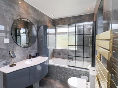 A bathroom with a bathtub, a round mirror, a sink with a cabinet, a toilet, and a heated towel rail at 315 Filey Road Scarborough