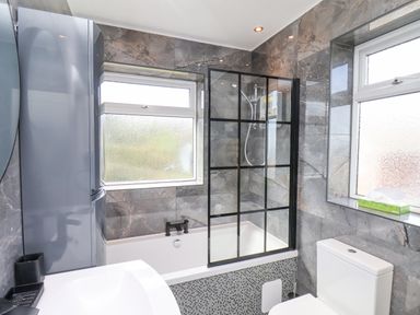 A bathroom with a bathtub and shower, toilet, sink, and two frosted windows at 315 Filey Road in Scarborough