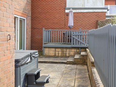 A patio area with steps leading to a raised deck with a table and closed umbrella behind a grey railing at 315 Filey Road in Scarborough