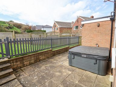 A backyard patio with a hot tub next to a brick wall and a fenced grassy area at 315 Filey Road in Scarborough