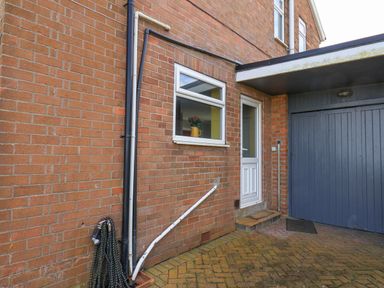 An outdoor area with a brick wall a hosepipe a small window with flowers a white door and a blue garage door at 315 Filey Road in Scarborough