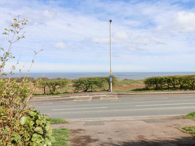 A road with a bus stop and bushes with fields and the sea in the background at 315 Filey Road in Scarborough